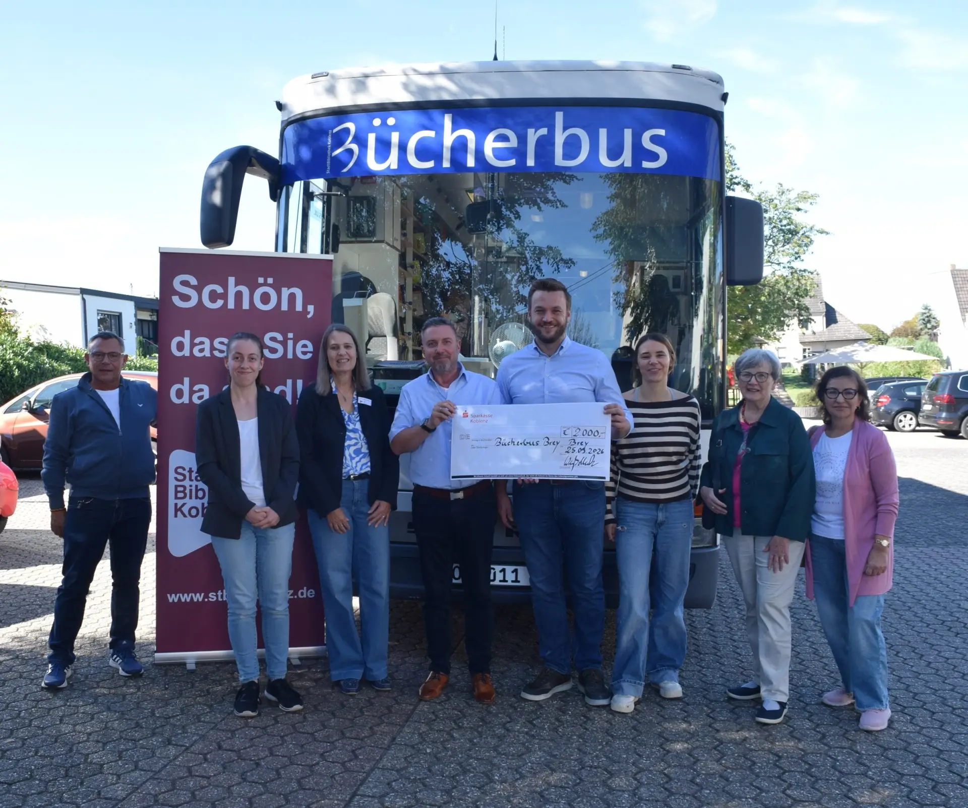Bücherbus der Stadtbibliothek Koblenz steht auf dem Dorfplatz in Brey, umgeben von Kindern, Familien und Erwachsenen, die das Angebot begutachten.
