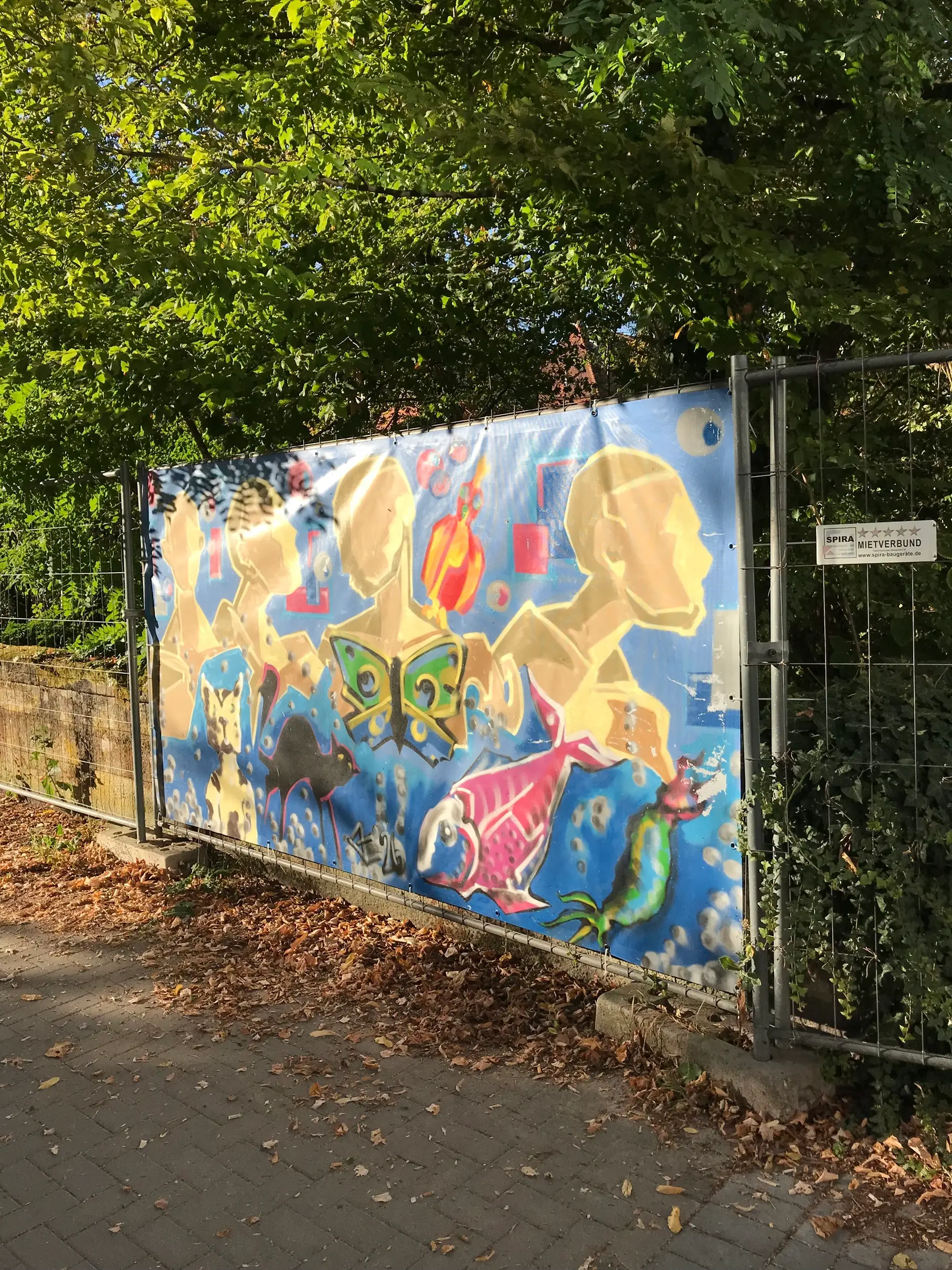Zwei Jugendliche bzw. Personen stehen bzw. halten sich an einem farbigen Bauzaunbanner mit Graffiti an einer Baustelle in Speyer.